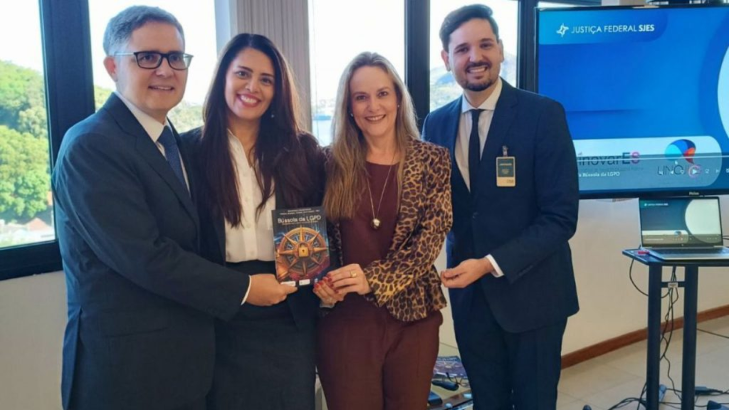 Imagem de dois homens e duas mulheres (elas ao centro) sorrindo e segurando o guia impresso