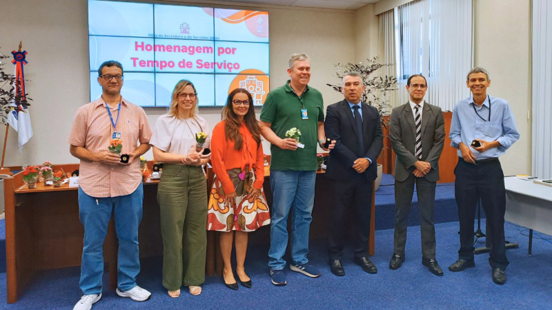 Fotos posada de duas mulheres e cinco homens. Homenageadas e homenageados mostram as caixinhas com os bótons recebidos