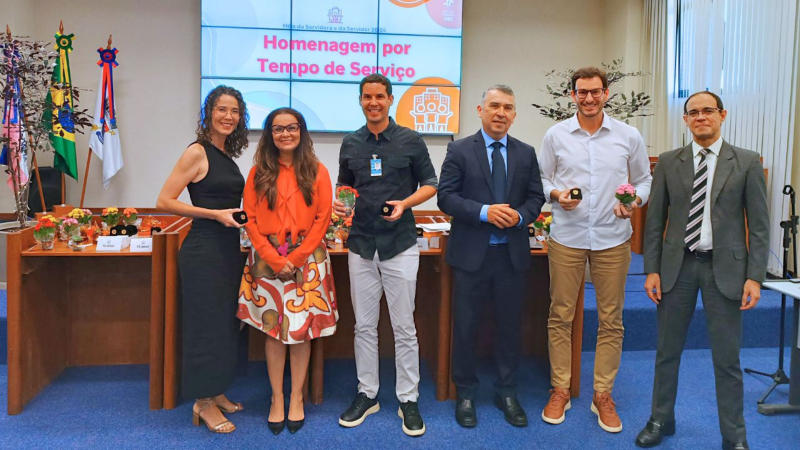 Foto posada de duas mulheres e quatro homens, sendo que uma das mulheres e dois dois homens seguram nas mãos caixinhas com os bótons recebidos