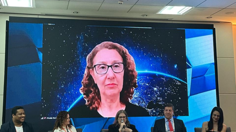 A laboratorista Neidy apresentando o painel, sentada, ao lado de dois homens e duas mulheres, Ao fundo, telão com imagem de outra painelista