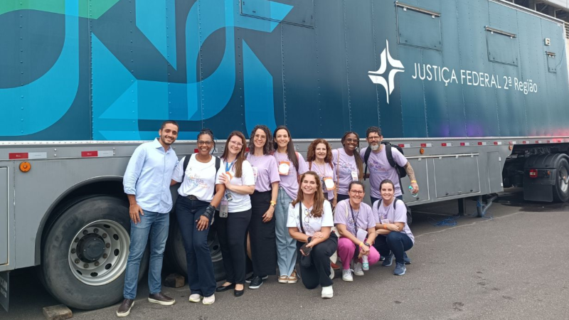 Grupo de voluntários do Mutirão PopRuaJud posando em frente à unidade móvel da Justiça Federal da 2ª Região, sorrindo para a foto.