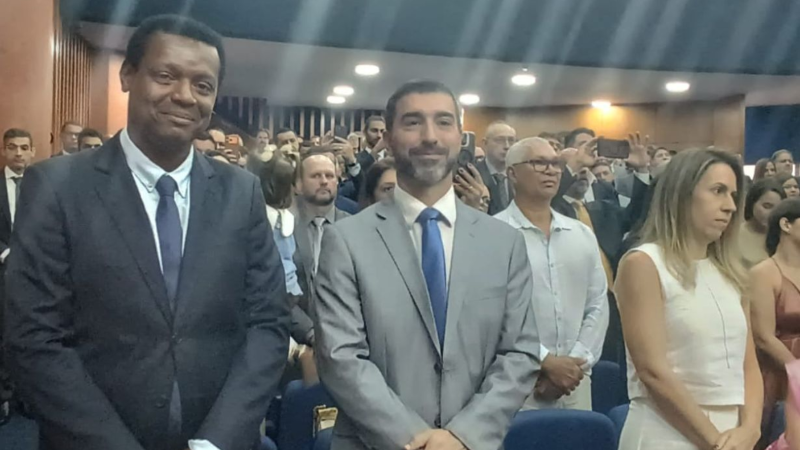 Autoridades de pé, no auditório, num determinado momento da solenidade. Um deles sorri discretamente para a câmera