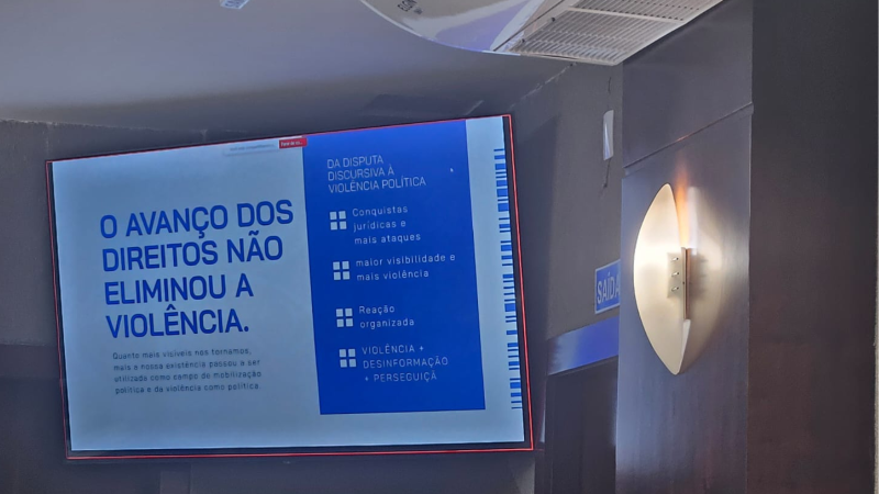 Telão na parede de frente do auditório, com a frase: "O avanço dos direitos não eliminou a violência"