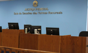 #PraTodosVerem: Imagem da Sala de Sessões das Turmas Recursais da Justiça Federal. O ambiente possui paredes azuis, bancada de madeira com computadores e cadeiras utilizadas durante as sessões de julgamento. Ao fundo, estão o brasão da República e a inscrição “Justiça Federal – Sala de Sessões das Turmas Recursais”.