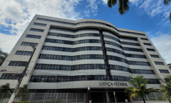 Fachada da sede da Justiça Federal, em Vitória: prédio de oito andares, mais horizontal que vertical, com formas curvas e janelas de vidro. 