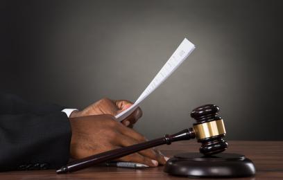 Mãos de magistrado negro segurando um documento. Ao lado, um martelo.  