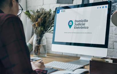 Imagem de uma mulher olhando para um PC. Na tela, o banner do Domicílio Judicial Eletrônico