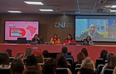 mesa com mulheres sentadas. ao fundo telão com imagem de mulher negra