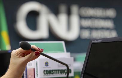 Mulher segurando microfone. Ao fundo, a logomarca do CNJ