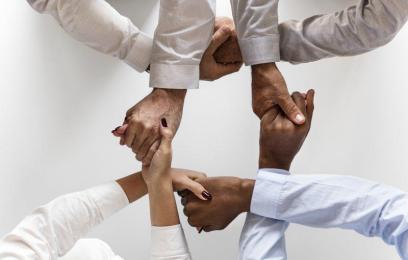 Imagem de mãos de pessoas de várias etnias, juntas, formando um círculo.