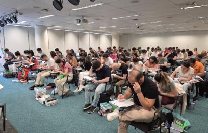 Sala de prova acarpetada, repleta de candidatos sentados em carteiras, fazendo a prova