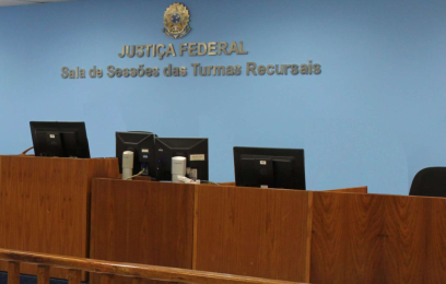 #PraTodosVerem: Imagem da Sala de Sessões das Turmas Recursais da Justiça Federal. O ambiente possui paredes azuis, bancada de madeira com computadores e cadeiras utilizadas durante as sessões de julgamento. Ao fundo, estão o brasão da República e a inscrição “Justiça Federal – Sala de Sessões das Turmas Recursais”.