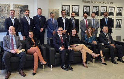 Grupo de magistrados e autoridades posando para foto em ambiente interno. Parte está sentada em sofás e parte em pé atrás, diante de uma parede com quadros de ex-diretores do foro. Todos vestem trajes formais.