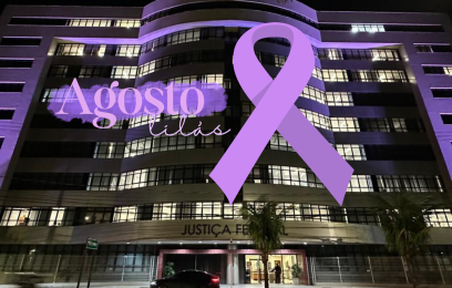 Fachada da sede da Justiça Federal, em Vitória, iluminada de lilás. Por cima da foto, um laço lilás e o texto "Agosto Lilás"