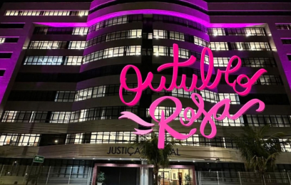 Fachada da sede da Justiça Federal, em Vitória, com iluminação na cor rosa. Sobre a foto, o texto "Outubro Rosa", em letras também cor-de-rosa