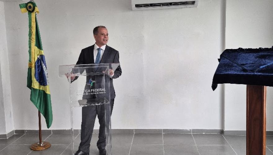 Homem de cabelo curto grisalho usando terno escuro fala atrás de um púlpito transparente