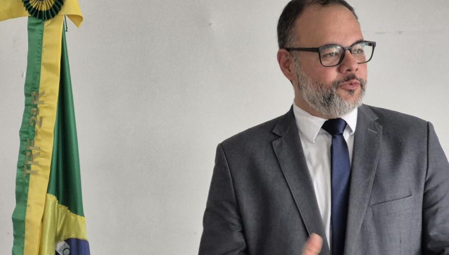 Homem de cabelo curto grisalho usando terno escuro fala atrás de um púlpito transparente