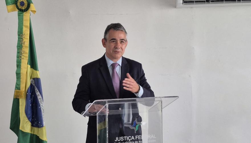 Homem de cabelo curto grisalho usando terno escuro fala atrás de um púlpito transparente