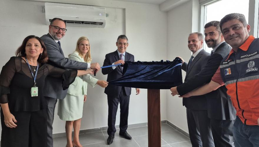 Homens e mulheres de pé descerrando uma placa coberta com tecido azul escuro